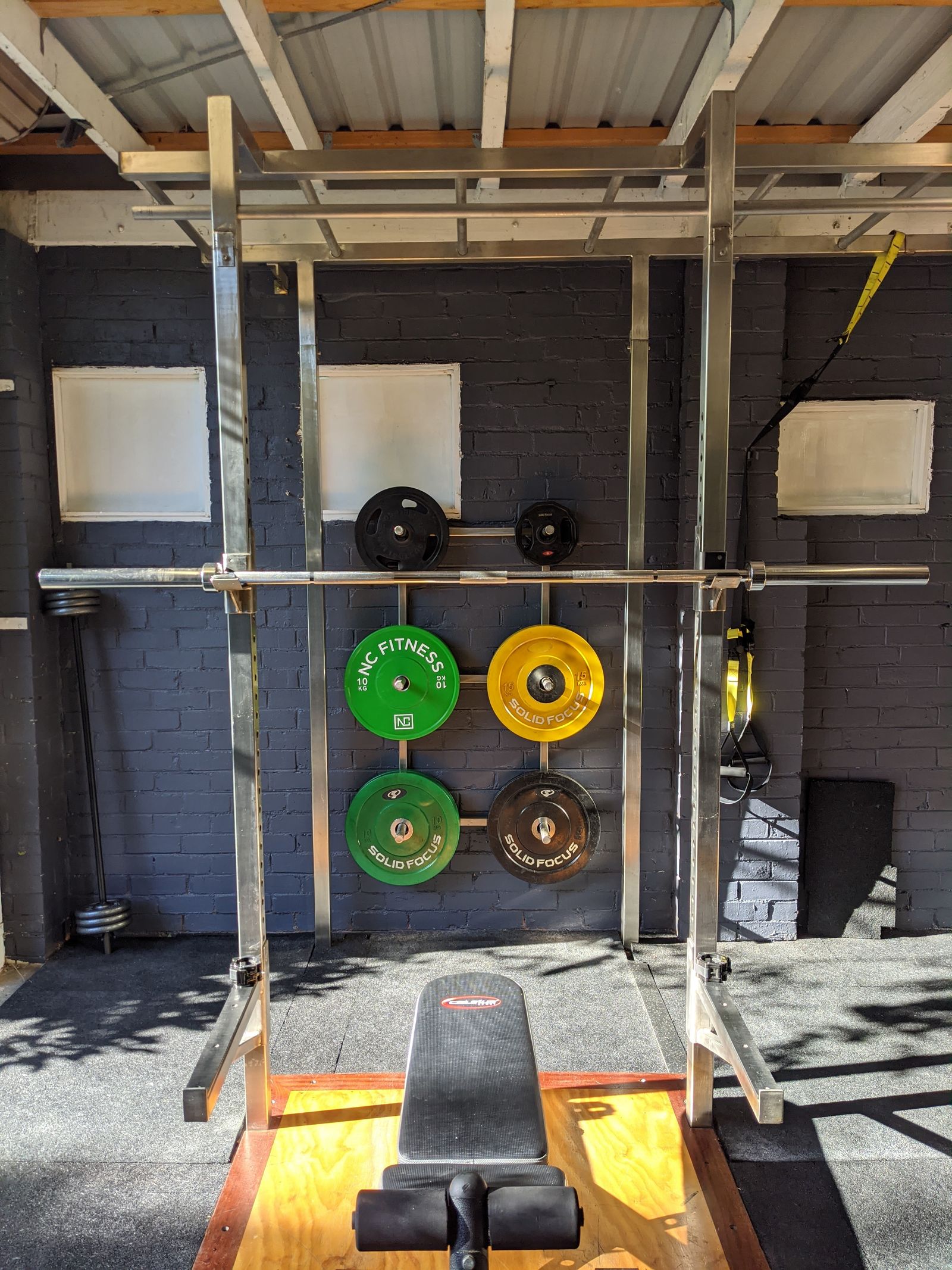 A home gym with a squat rack, barbell, weight plates and a bench