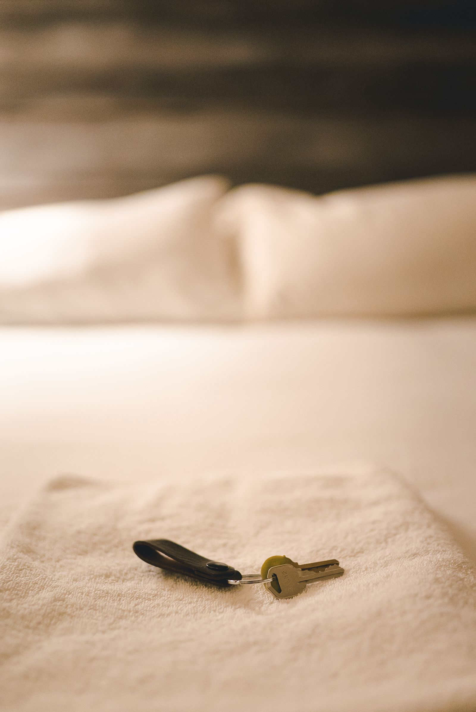 Folded white towel with a set of keys laid on a freshly made bed