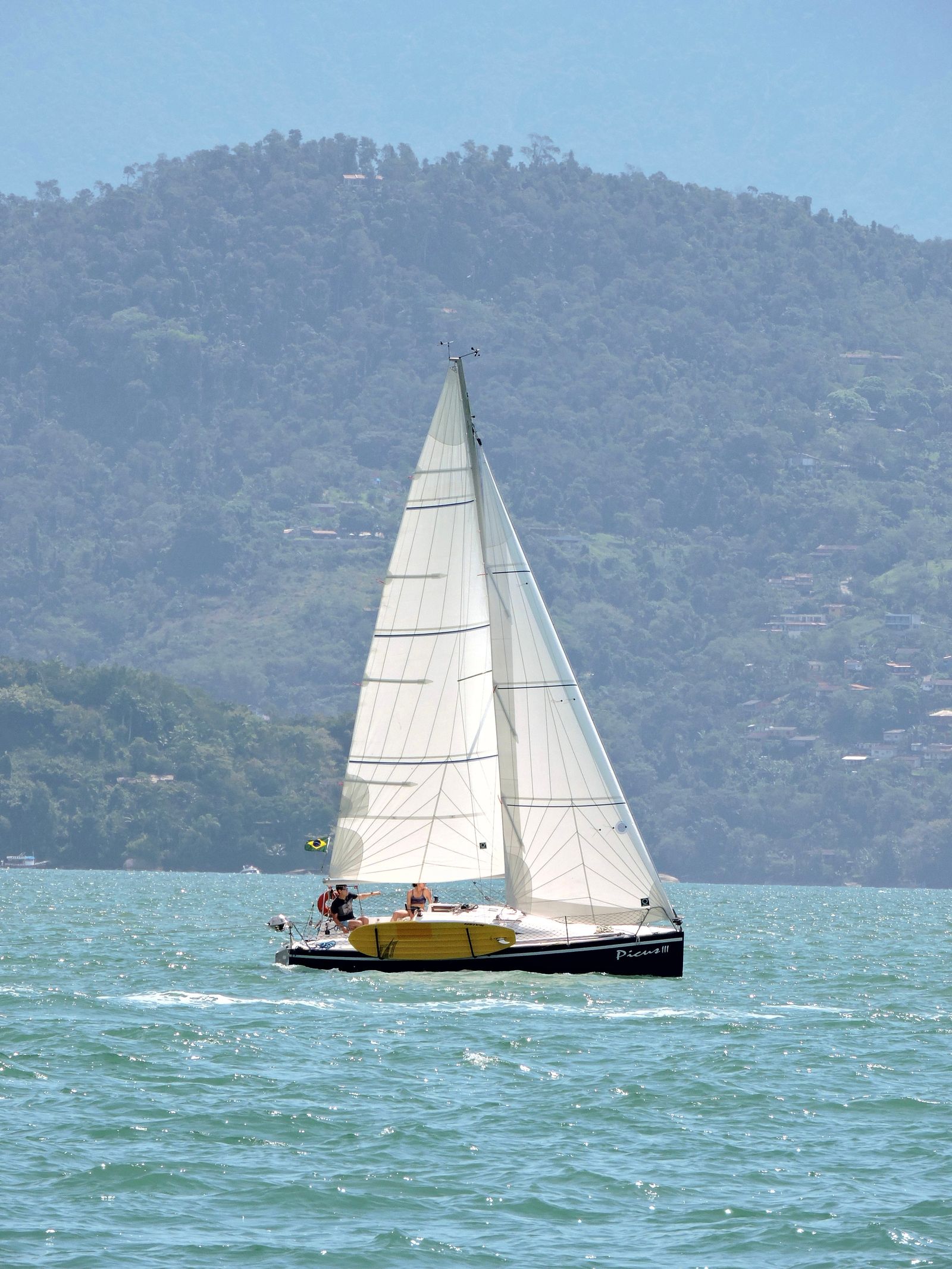 Sailboat with white sails on turquoise water in front of mountains