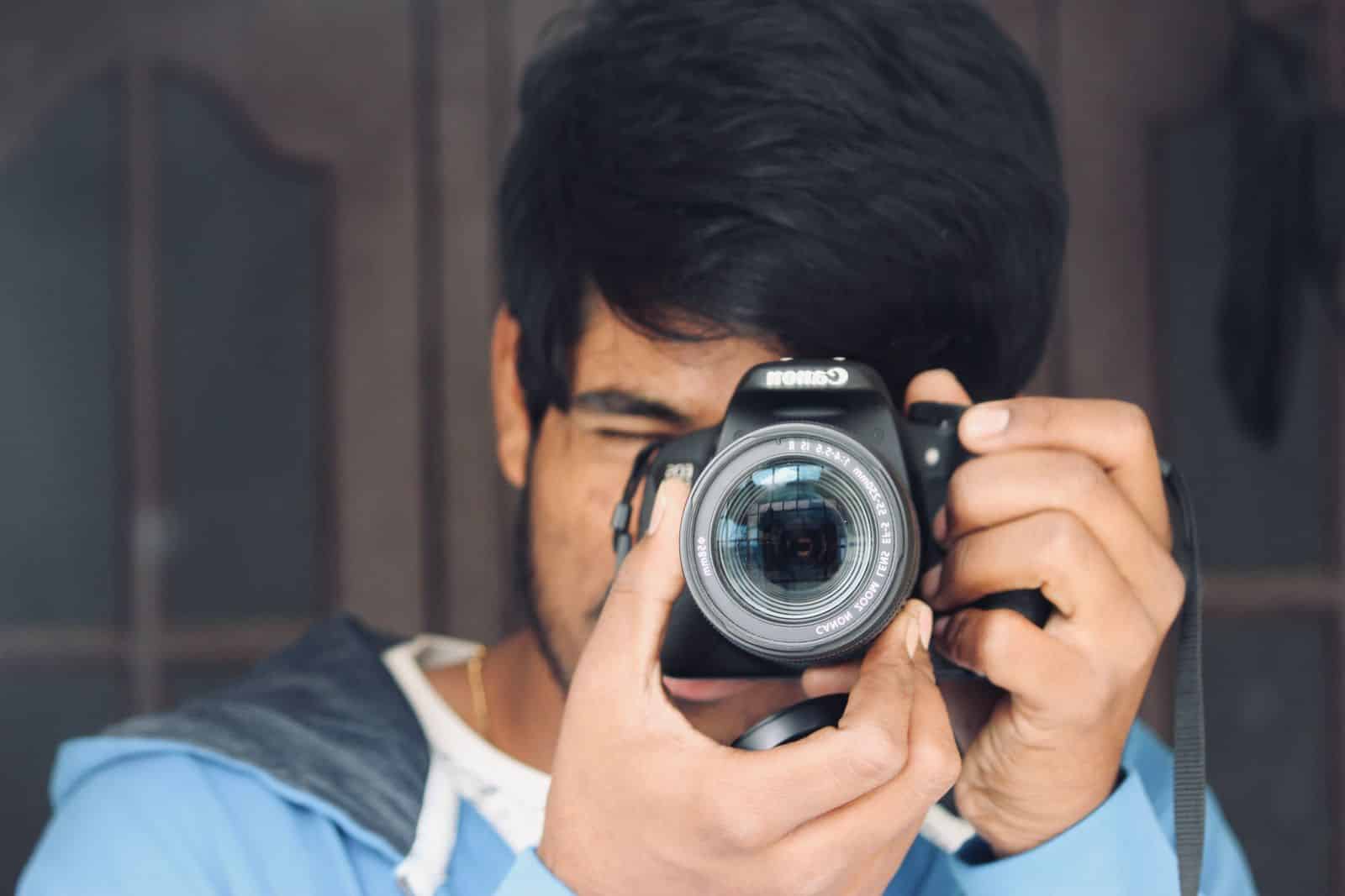 Young man concentrating while taking a photo with a DSLR camera indoors